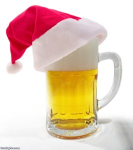 A glass beer mug filled with beer, topped with foam and adorned with a red santa hat against a white background.