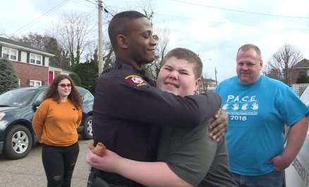 A police officer hugging a boy in front of people.