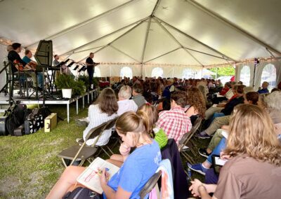 A large crowd of people sitting in chairs under an awning.