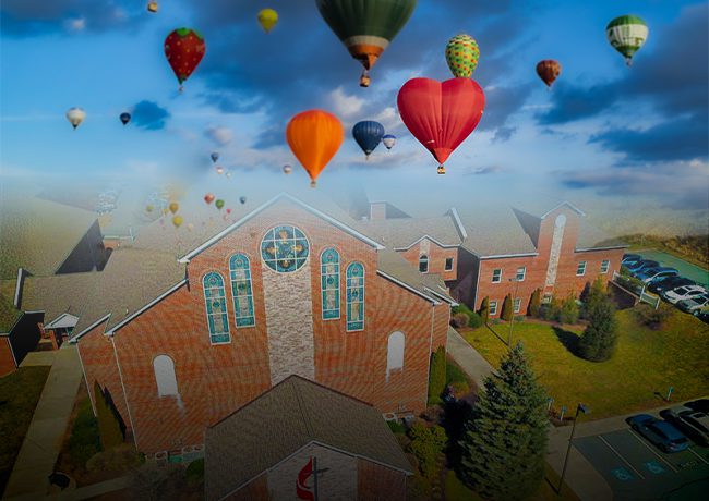 A group of balloons flying over a church.