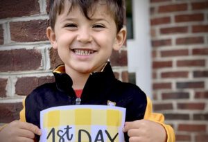 A boy holding up a sign that says " 1 st day of school ".