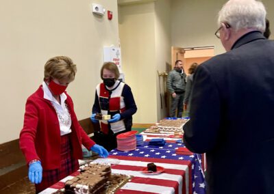 Masked volunteers serving desserts at flag-draped table